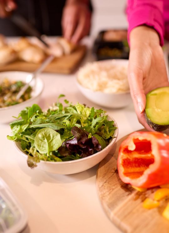 Close Up Of Couple In Kitchen Wearing Fitness Clothing Making Batch Of Healthy Meals For Freezer